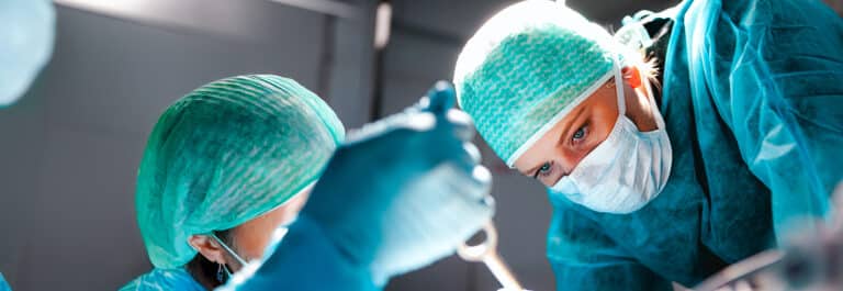 Close up of surgeon in surgery room wearing blue scrubs under bright light.