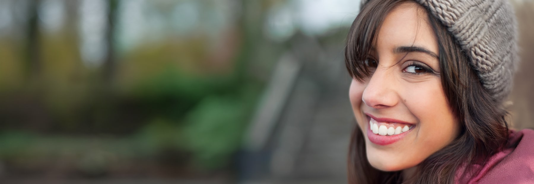 Brown-hair-young-person with bangs, smiling at camera wearing gray beanie hat.