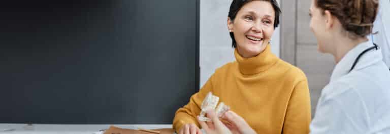 Person with short hair in yellow turtleneck sweater engaged in conversation with doctor holding model of teeth.