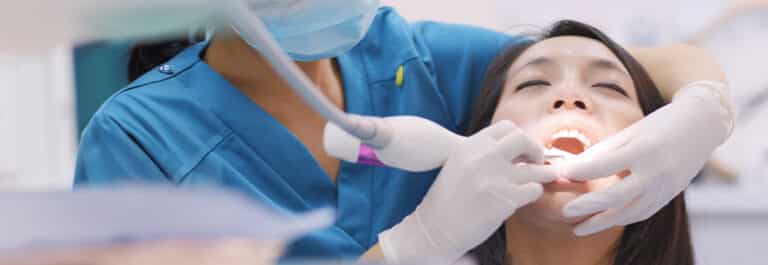 Close up of doctor with medical gloves performing periodontal cleaning on patient.