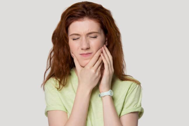 Red-headed woman holding jaw from tooth pain.