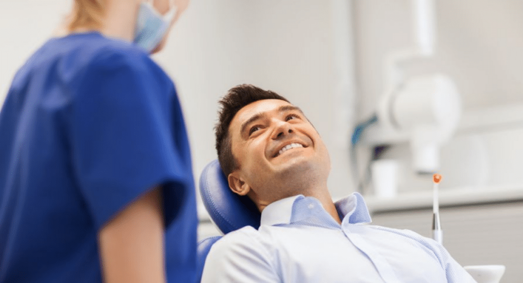 Male patient in dentist chair smiling at dental assistant.