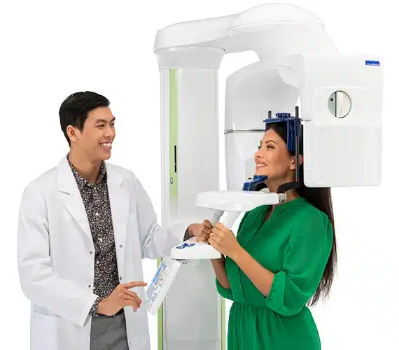 Patient in green outfit standing under Cone Beam x-ray machine.