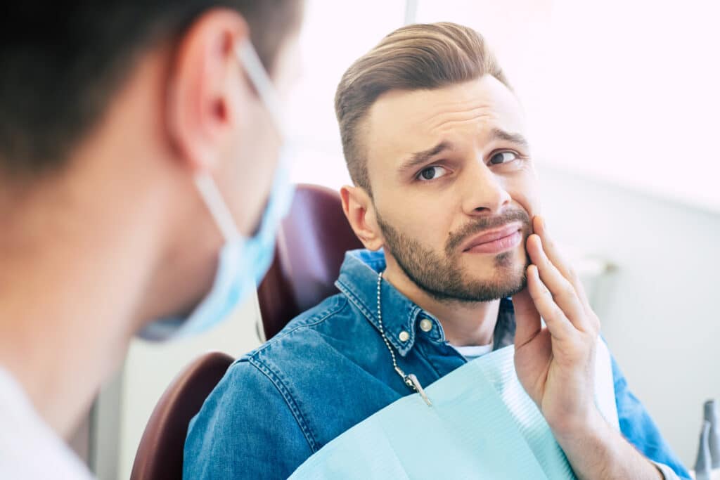 Patient with facial hair, holding face due to root canal pain.