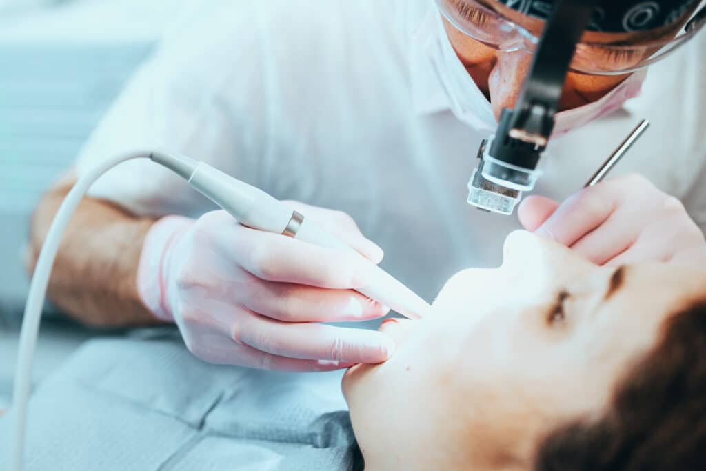 Dentist cleaning out dental canal using tool in patient's mouth.