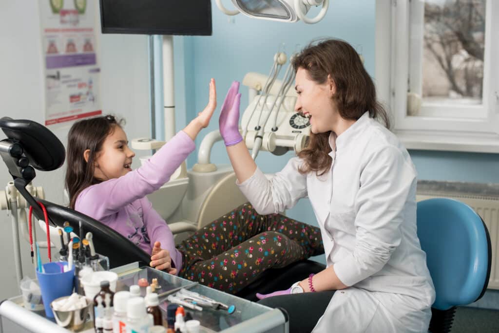 Dentist high-fiving kid smiling in dental clinic office.