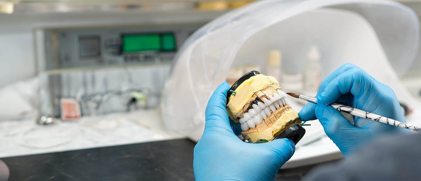 Doctor wearing blue latex gloves holding model of teeth with dental instrument in hand.