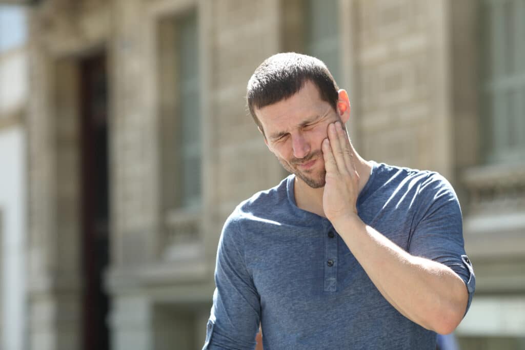 Person with short hair on street suffering from tooth ache.